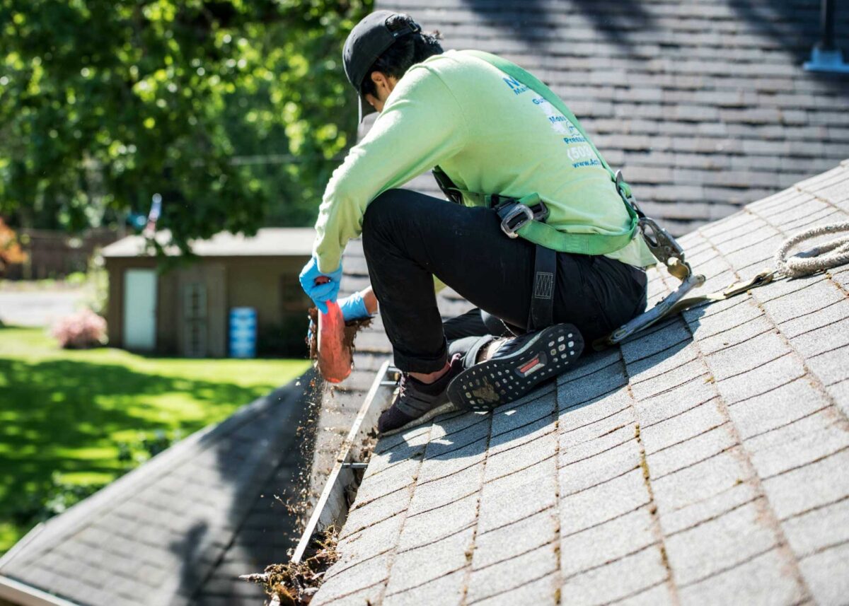 About Gold Coast Gutter Cleaning, Worker wearing green long sleeved shirt cleaning gutters